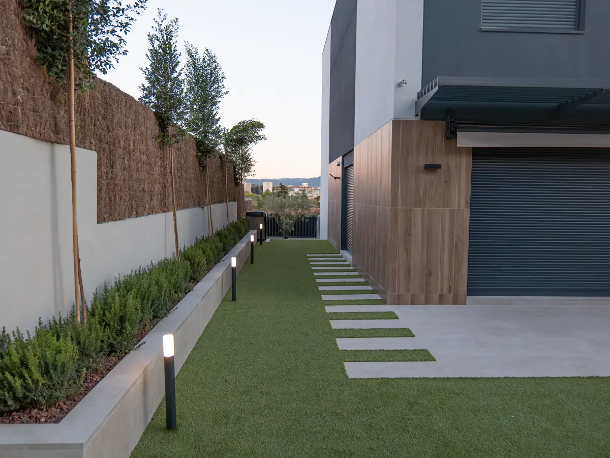 Recorrido exterior con balizas iluminadas junto a vegetacion y paso de losas
